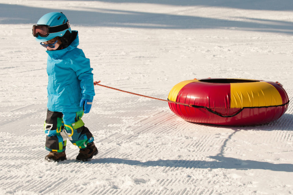 Boy pulling a snow tube dressed in warm winter clothing, one of the tips for snow tubing with kids