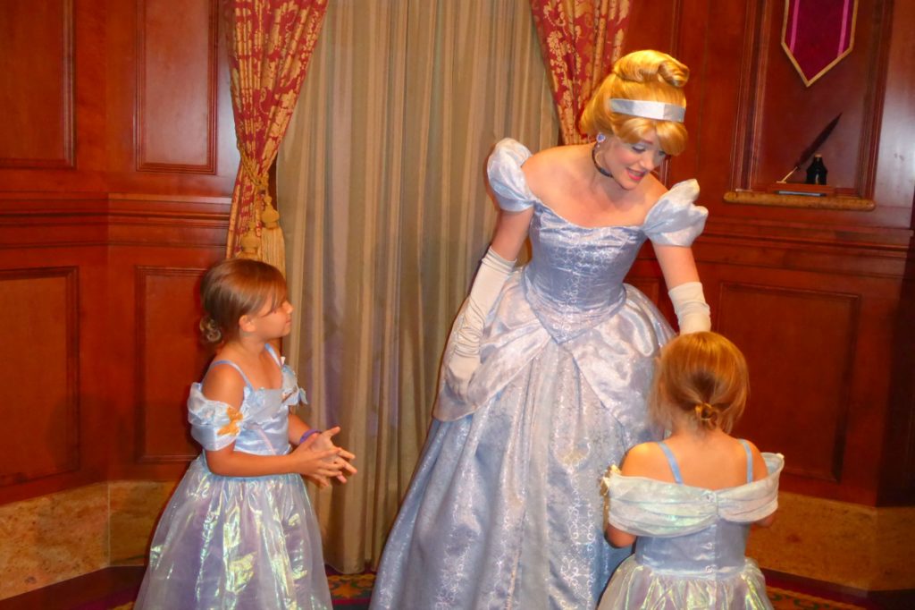 two little girls chat with cinderella at a disney character meeting. they are wearing dresses that match hers.