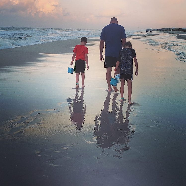 father and sons collecting seashells at sunset on the beach
