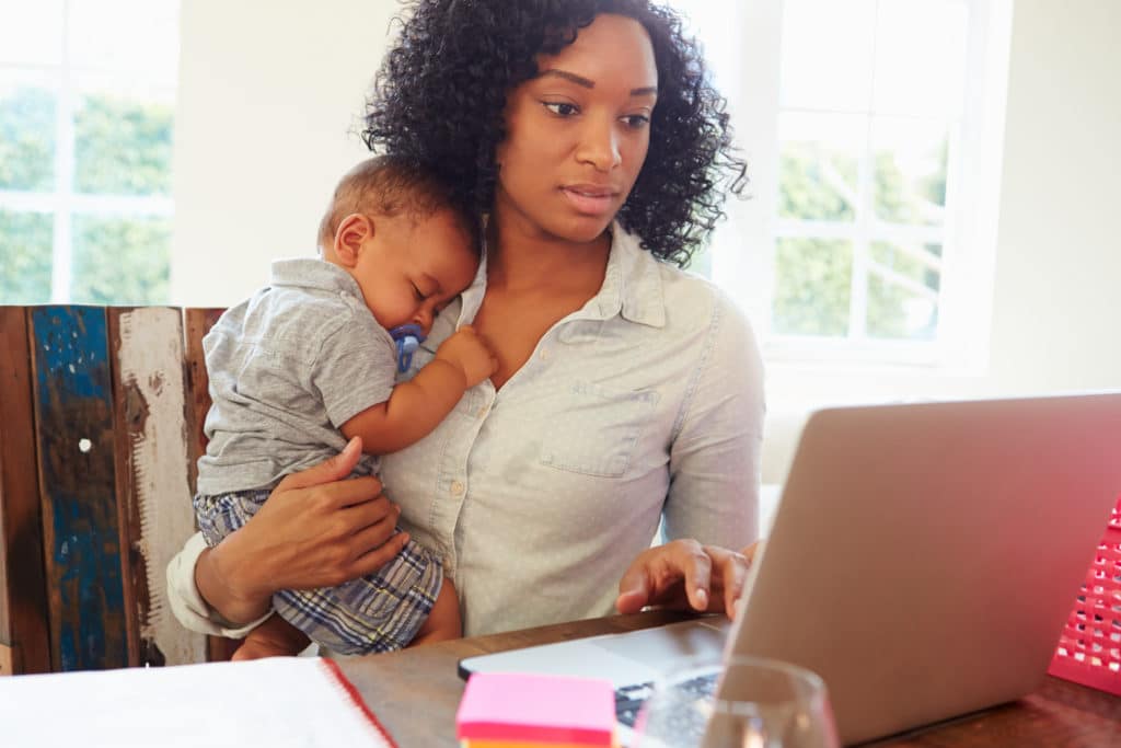 mother working from home on laptop holding baby