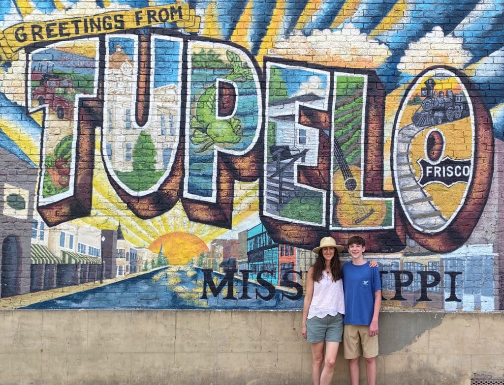 Woman and teen boy standing in front of the Greetings from Tupelo mural