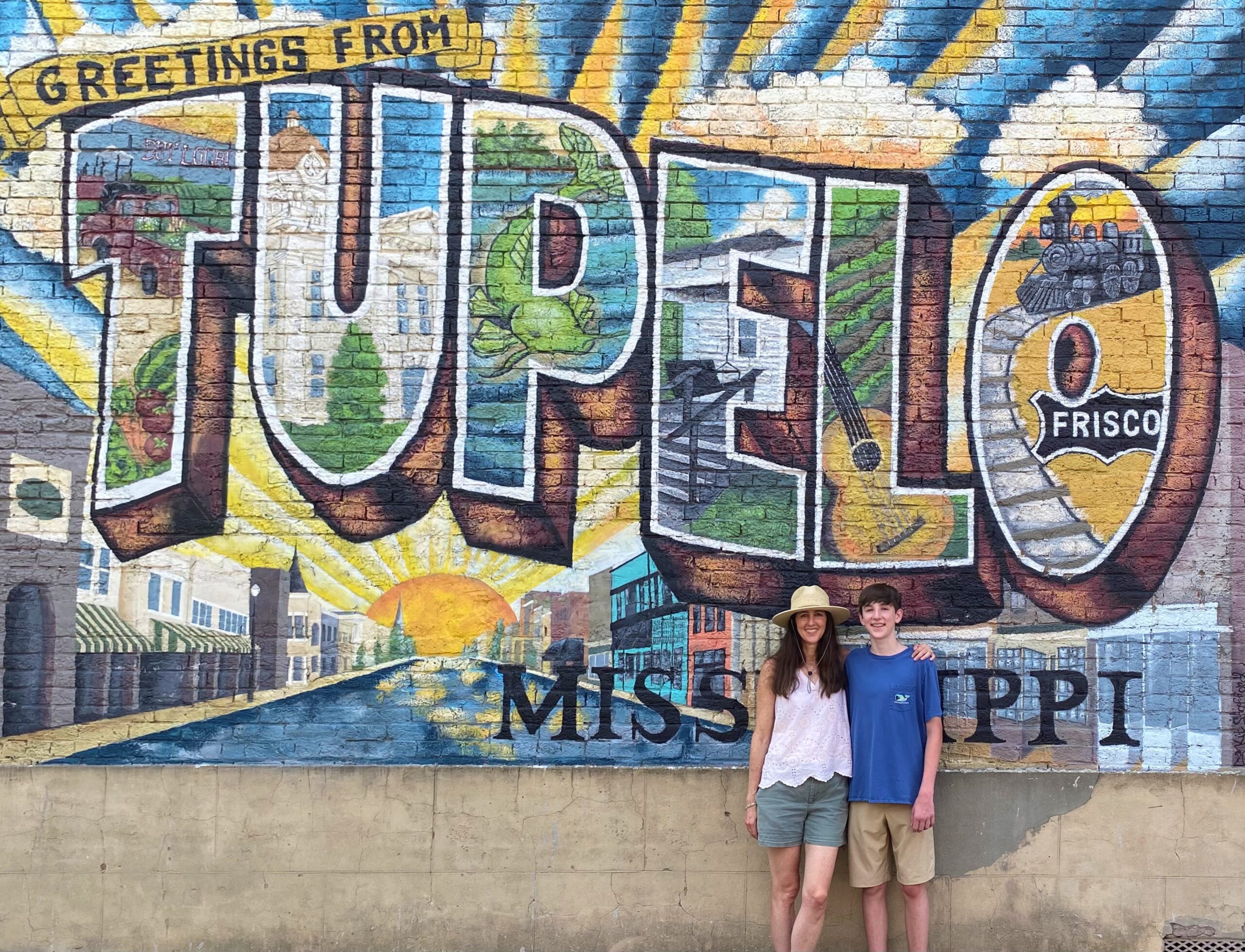 Woman and teen boy standing in front of the Greetings from Tupelo mural