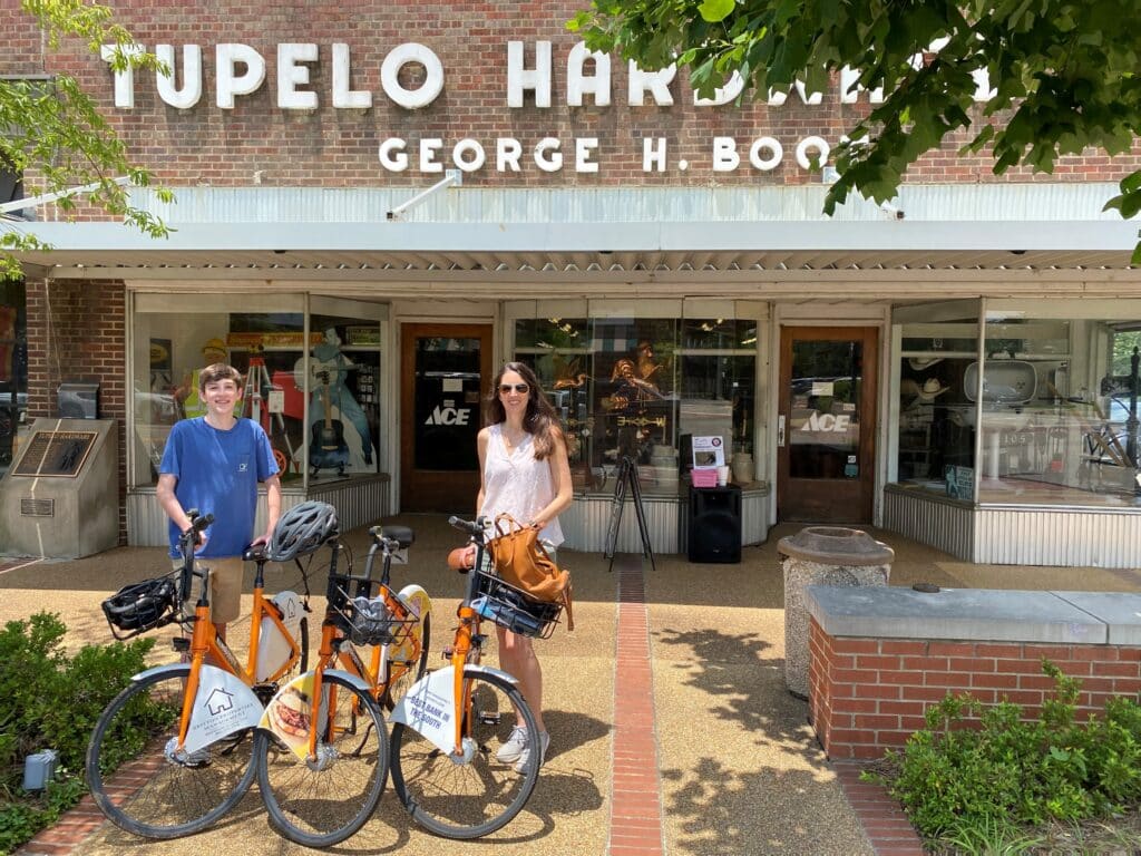 Woman and teen boy on bikes in front of Tupelo Hardware Co.