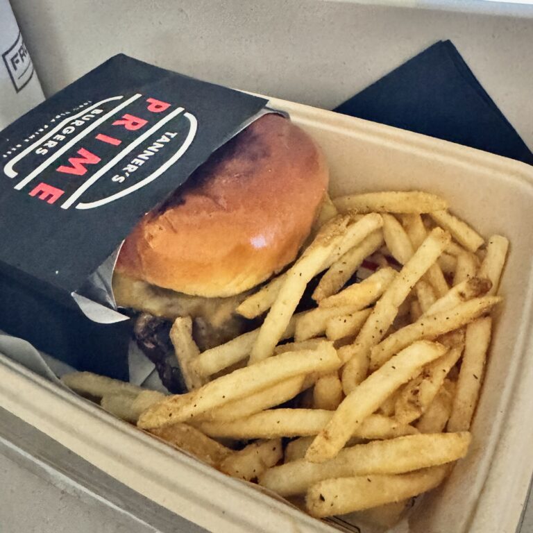 Hamburger and fries in a tray. The burger is in a sleeve that reads Tanner's Prime Squeeze.
