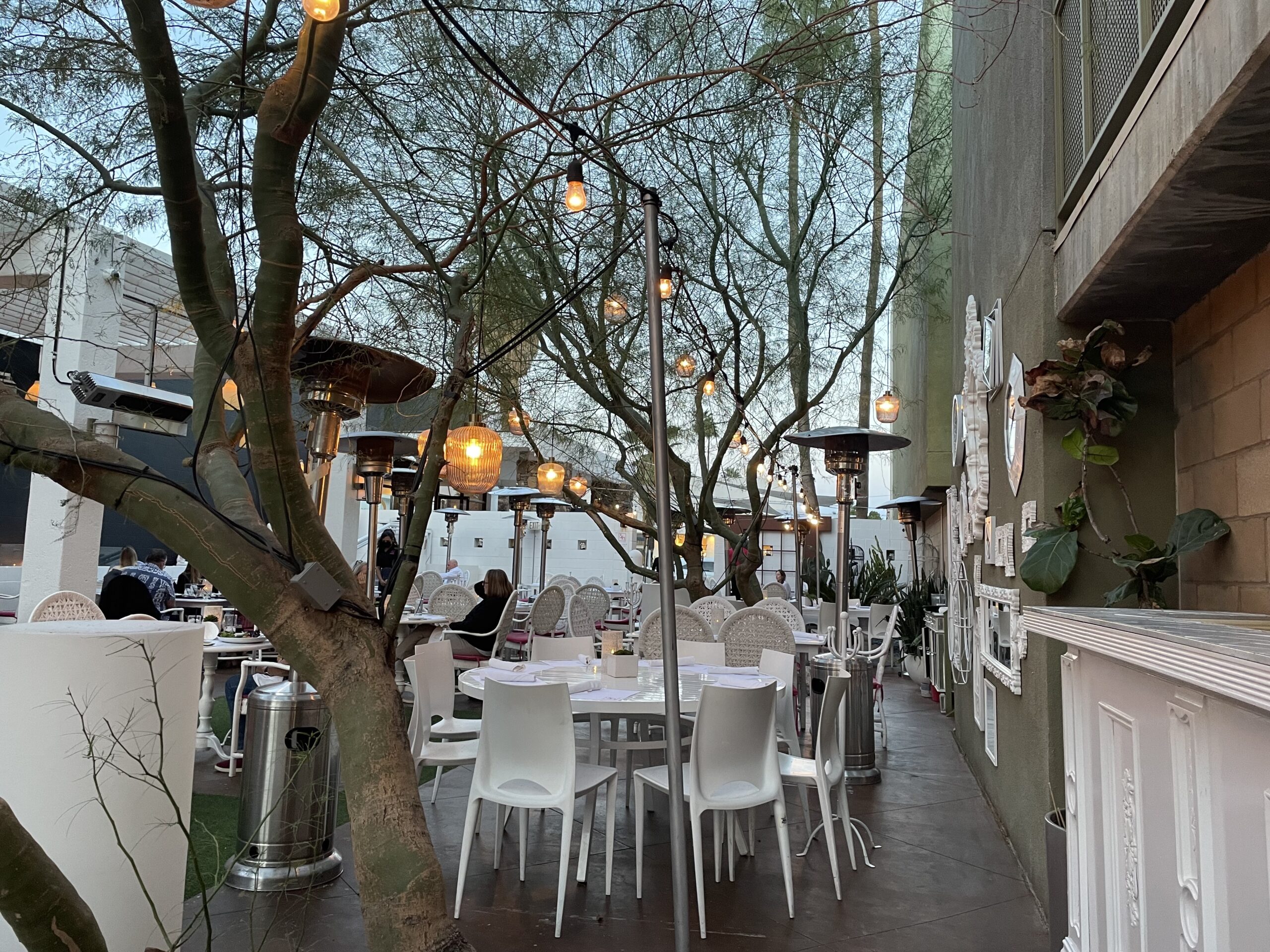 Outdoor patio with overhead lights and white bistro tables at Eight4Nine, a great place to eat in Palm Springs