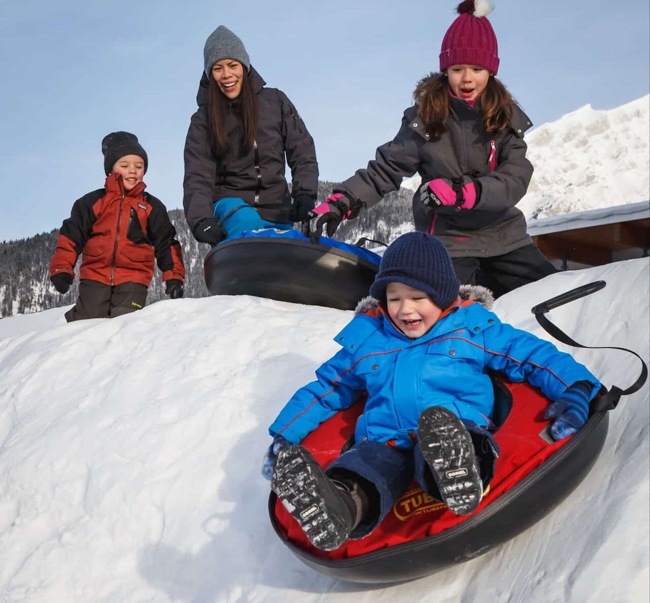 Family at top of hill sending child tubing down the slope, one reason why winter is a best time to visit Banff.