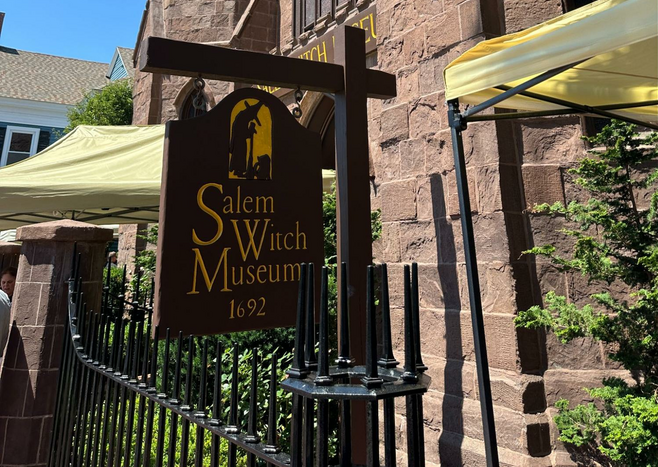 View of the outside of the Salem Witch museum and its sign. Two modern tends provide shade in front.