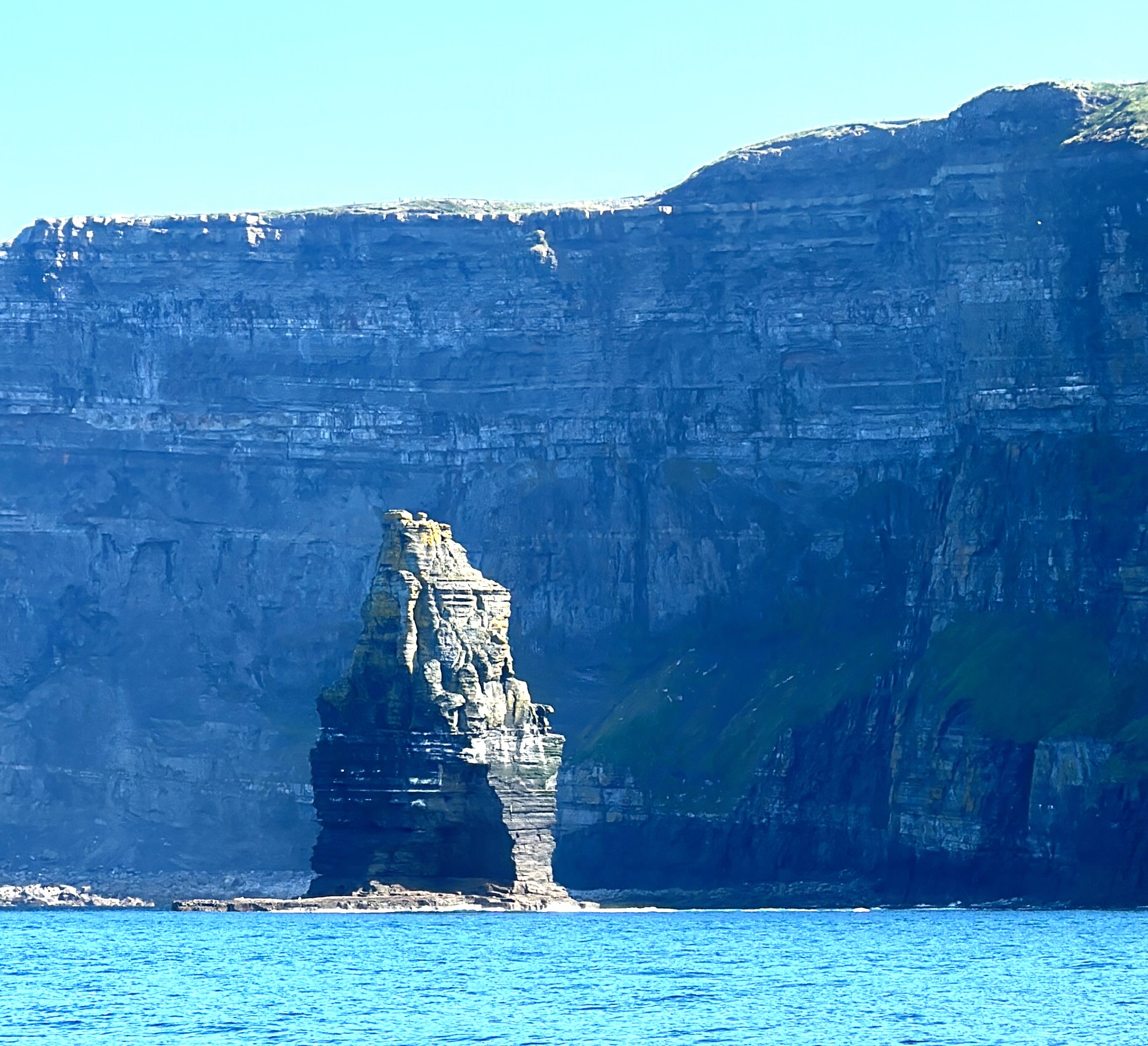 View of Sea Stack at the Cliffs of Moher from the water. A stack of stone stands apart from and in front of the cliff face.