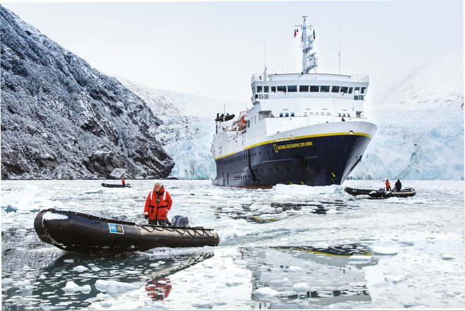 Cruise ship making it way through ice filled channel with rafts exploring around it.