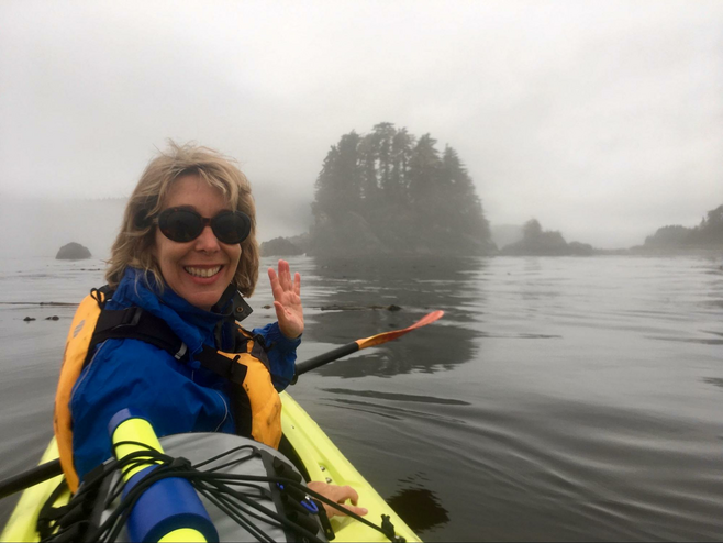 The author waving to camera on a kayak in foggy Alaska inlet.
