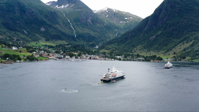 Cruise ship moored in fjord by small Norwegian village.