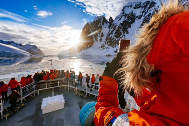 Bundled up passenger taking photo off bow of ship as ship traverses channel