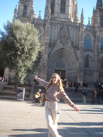 Hudson smiling with her arms out wide in front of the Barcelona cathedral.