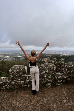 Hudson standing with her arms up looking out from the top of a castle in Sintra, Portugal.