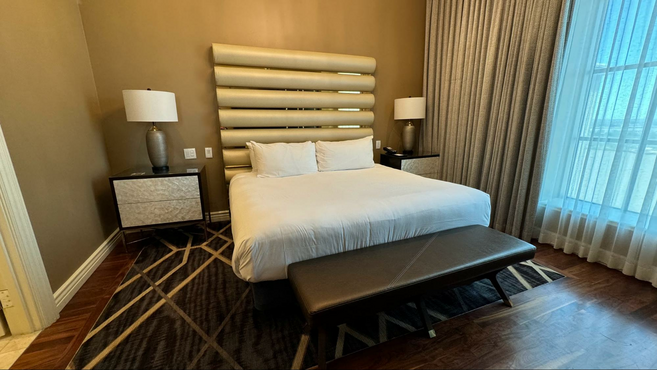 Hotel room at with bed in the middle next to a bed, two nightstands and a window.
