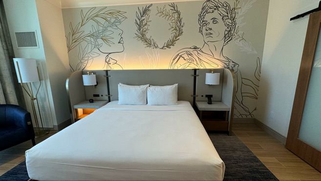 Hotel room with full size bed and sketch decor of Julius Caesar on the wall.