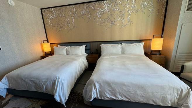 Two beds inside a dimly lit room with a floral backboard and yellow lamps.