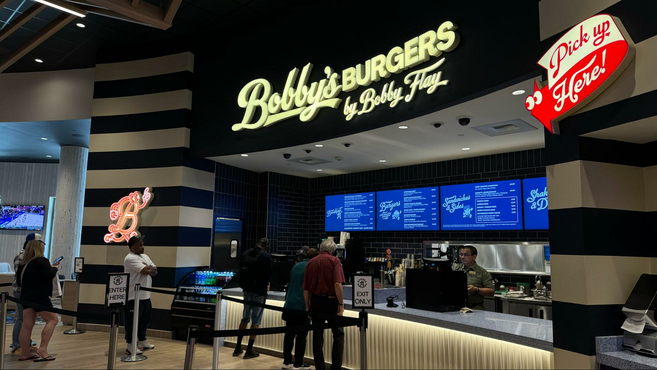 White Bobby's Burgers sign and line of people waiting to order food inside of the food hall. 