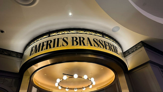 The words Emeril's Brasserie against a well lit glass backing and a circular lighting fixture.