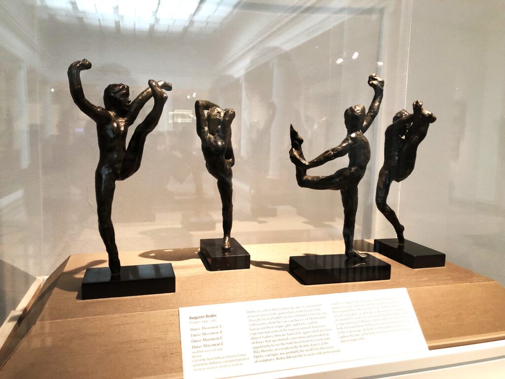 Four bronze sculptures in a glass display case. Each depicts a dancer holding a dance position. There is a placard explaining the display in front.