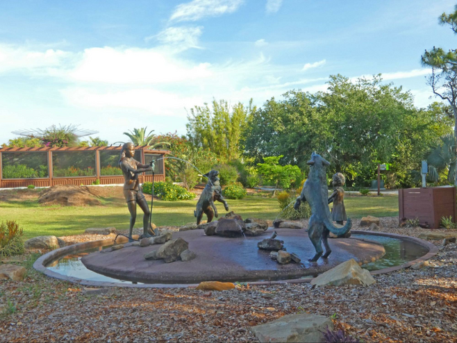 A sculpture of woman  and child hosing and two dogs playing in the water.