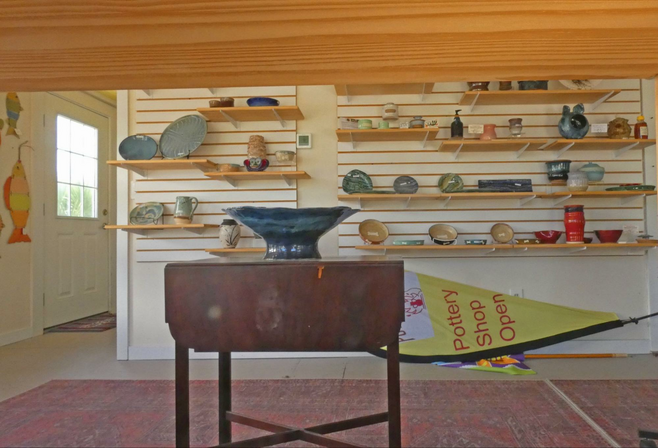 A pottery shop with pottery on shelves and table with pottery on it in front.