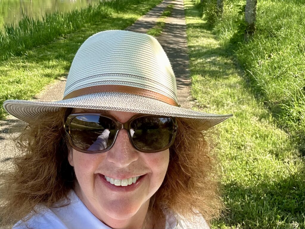 Woman wearing a Wallaroo hat and sunglasses on a towpath beside a canal in Burgundy.