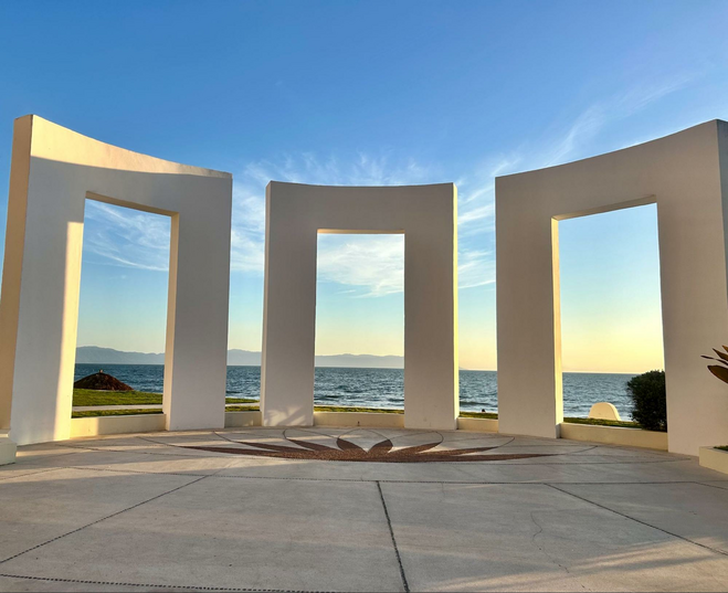 Three elongated archways towering outside, with the pacific ocean in the background and clear skies