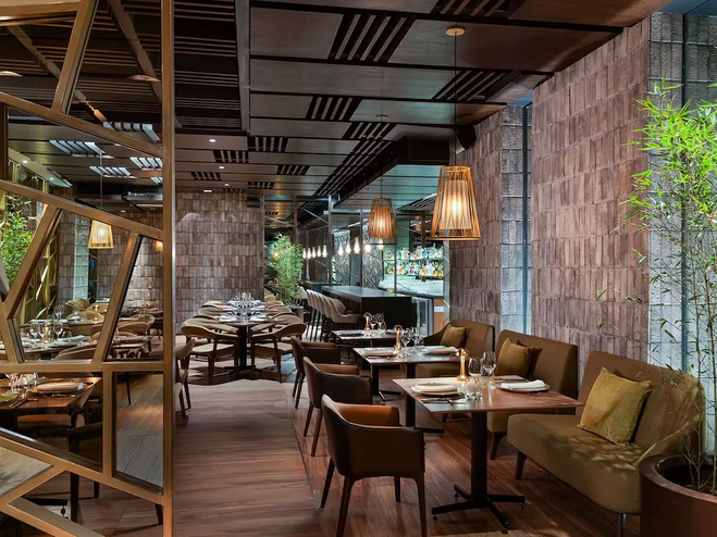 Inside Sen Lin with a warm design featuring wood accents, comfy chairs, and soft lighting. The space has tables with simple settings, bamboo plants, and hanging lights