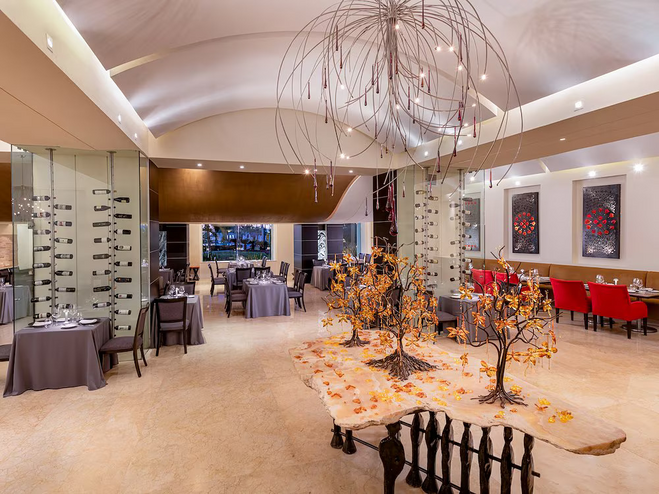 Inside Piaf restaurant, French-inspired design with rich red and gold tones, elegant table settings, and soft ambient lighting, with curved seating, artistic decor, and a romantic atmosphere