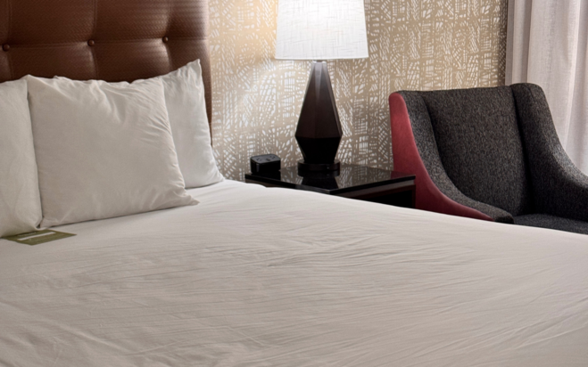room with chair, table with light, bed that is made with pillows