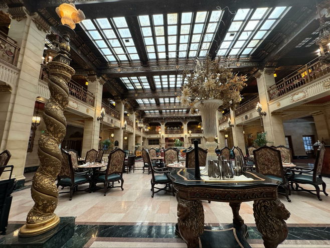 Large ornate room with a ceiling of skylights, heavy wood dining furniture and ornate artworks.