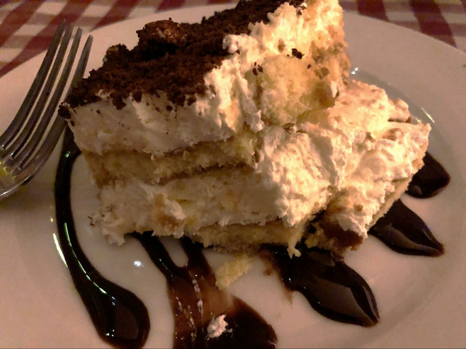 Tiramisu Dessert on a plate with a fork and drizzled with chocolate sauce.