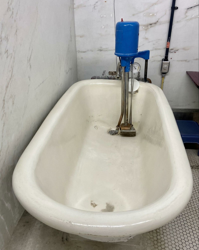 Tall sided calcium stained white tub with plumbing historic plumbing inside a tiled bathroom.