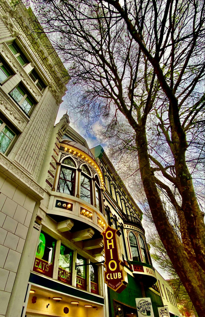 The exterior of a victorian building with a vertical sign, many windows and banks of lights next to a tree lined street.