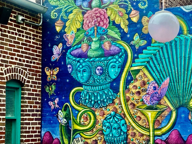 Colorful wall mural of butterflies and accordions, tubas and garden planters next to a brick building.