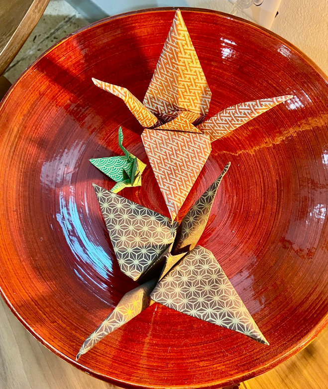 Paper folded in the shapes of birds in flight--traditional origami on a red plate.