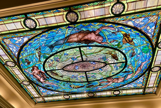 Mermaids floating in blue-hued stained glass ceiling artwork.