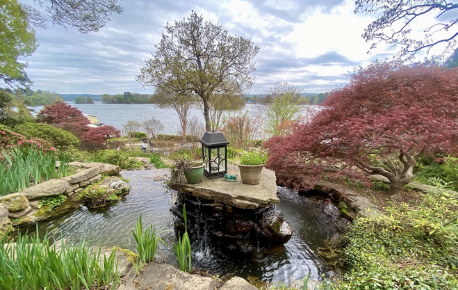 A Japanese-style garden with stacked stone, a lantern and bonsai-shaped trees and gently flowing pond overlooking the much larger lake.