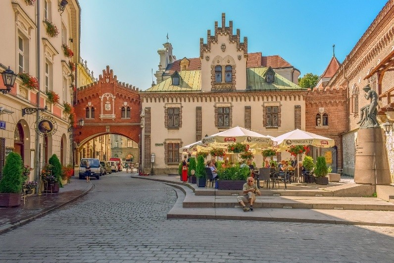 Historic buildings along a brick-paved street with outdoor cafe with tables and patrons sitting under umbrellas.