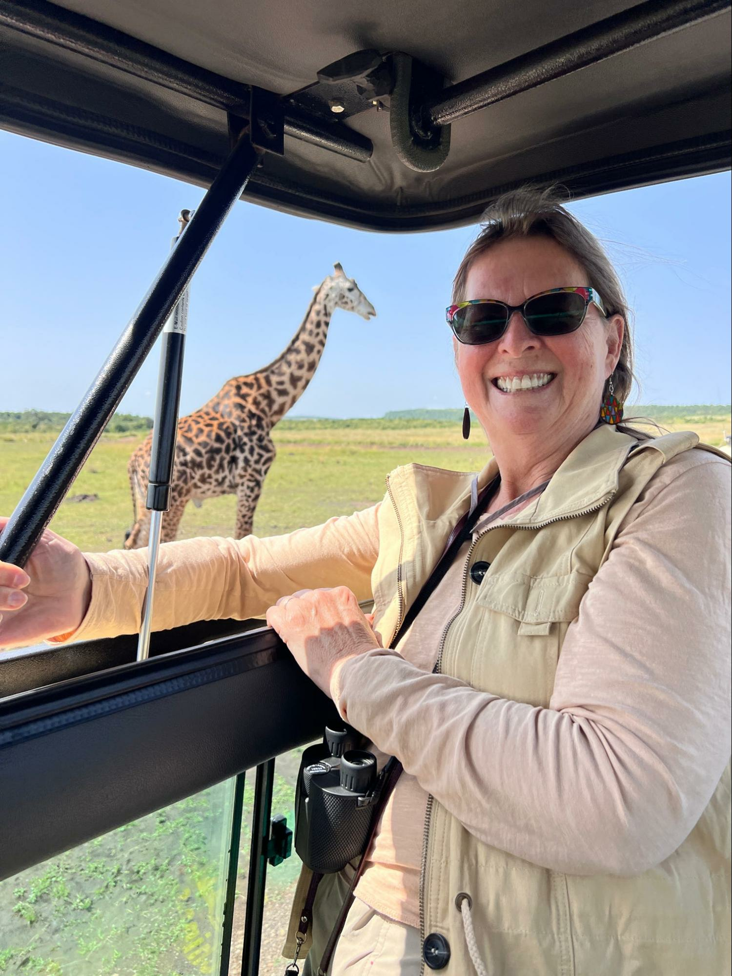 Woman posing in a safari truck with a giraffe in the background.