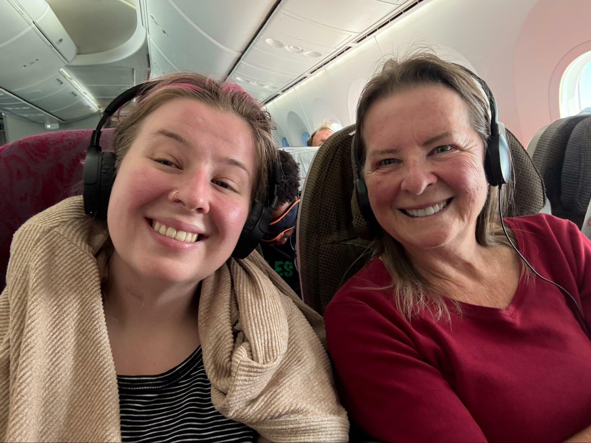 Two women in airplane seats wearing headphones on a long flight