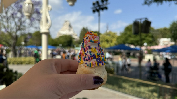 Hand holding a coconut macaroon with white chocolate and sprinkles with the matterhorn attraction in the background.