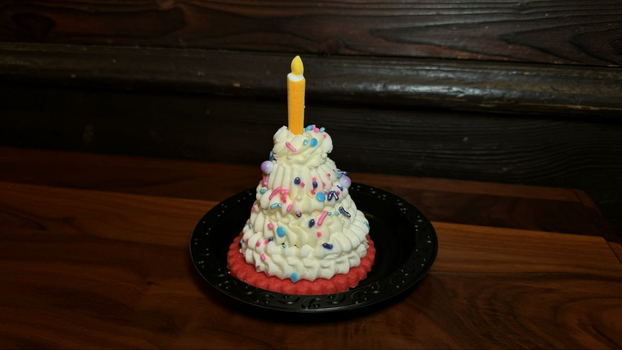 Pink shortbread cookie on a small black plate with a mound of white buttercream with sprinkles and a yellow sugar candle.