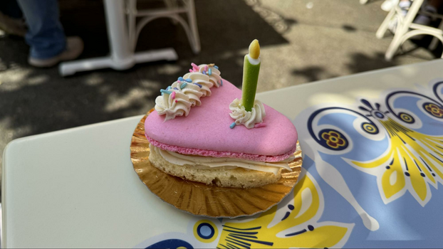 Pink cake looking macaron on a small gold plate with a green sugar candle.