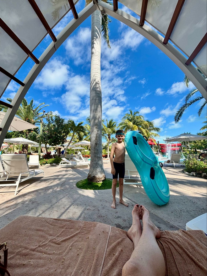View of the Beaches Resort waterpark in the background and a boy holding an inner tube from the perspective of a person sitting in a cabana reserved and outfitted by a Beaches butler.