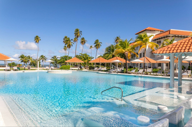 Blue pool with zero gravity entrance surrounded by cabanas and palm trees