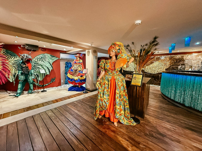 Mannequin in a yellow print carnivale costume dress with headdress standing in front of a bar