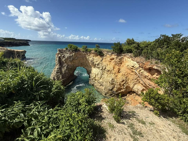 Rock formation arching over the blue water with island greenery in the forefront.
