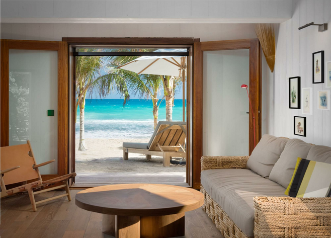 Living room with couch, chair, and table looking out onto the beach with blue water and lounge chairs